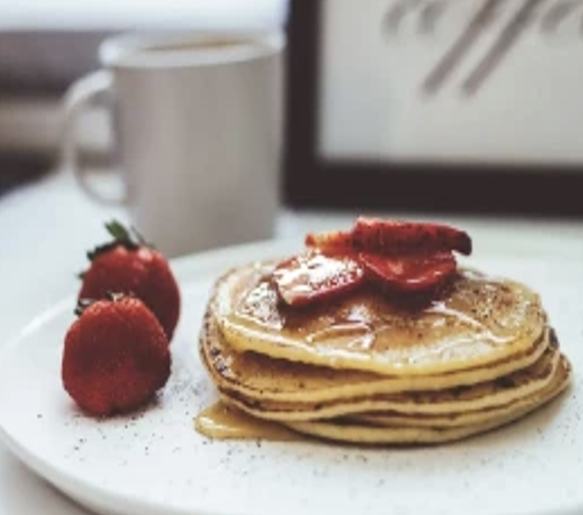 Four pancakes, one on top of the other. Two strawberries on the side.